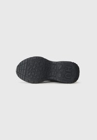 Semelle de chaussure en caoutchouc noir avec un motif de grip texturé, comportant des formes géométriques et un logo central. Talon incurvé pour un support supplémentaire.