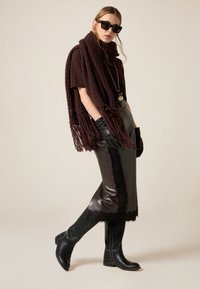 Sciarpa marrone lavorata a maglia con frange, top marrone a maniche corte, gonna in pelle nera con rifiniture in pizzo, guanti neri e stivali neri al ginocchio.