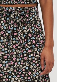 Svart blomstret skjørt med små hvite, rosa og blå blomster. Har en knyte i livet og myk, teksturert stoff.