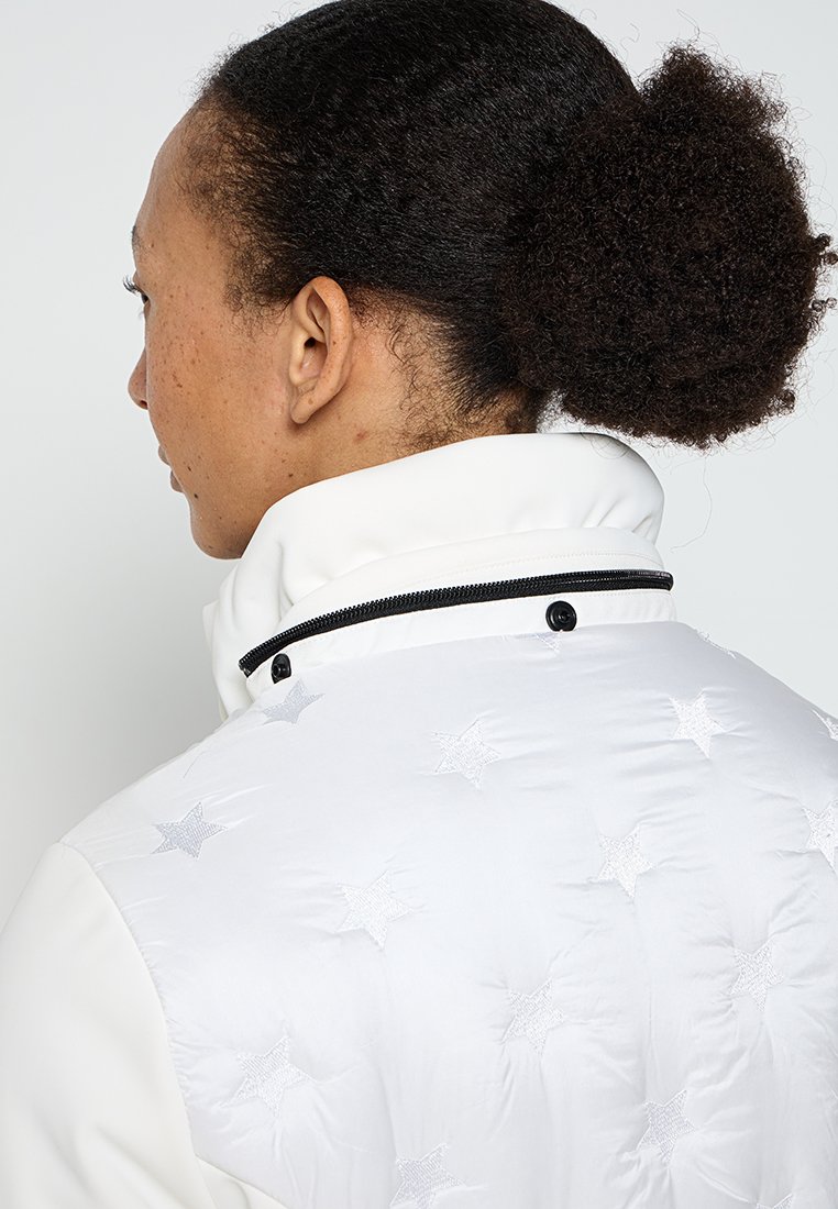 Giacca imbottita bianca con colletto alto, dettagli di cerniera nera e stelle argentate ricamate sul retro. Tessuto liscio con finitura lucida.