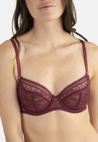 Soutien-gorge en dentelle bordeaux avec des détails brodés ; il présente des baleines, des bretelles réglables et des bords festonnés pour une texture.
