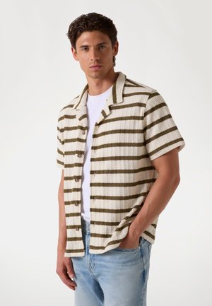 Chemise à manches courtes en tissu texturé, présentant des rayures horizontales beige et vert olive, un col camp, et une fermeture à boutons sur le devant.