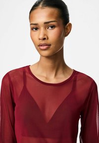 Burgundy transparent topp med rund halsringning och långa ärmar, med ett subtilt triangulärt mönster fram och en lätt, genomskinlig textur.