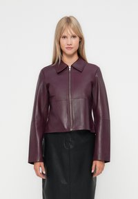 Veste en cuir bordeaux avec un col structuré, fermeture éclair à l'avant et manches longues. Associée à une jupe en cuir noire. Texture lisse.