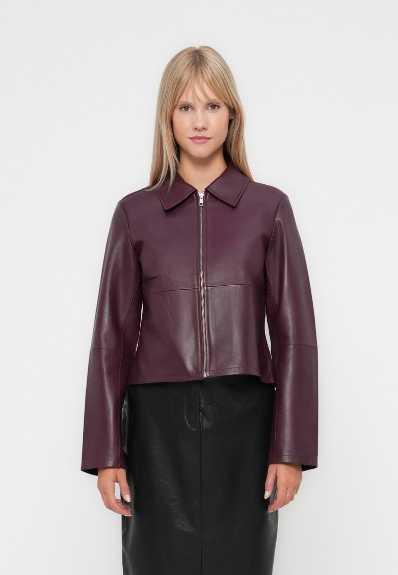 Veste en cuir bordeaux avec un col structuré, fermeture éclair à l'avant et manches longues. Associée à une jupe en cuir noire. Texture lisse.