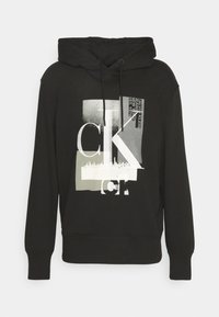 Felpa nera con grafica frontale che presenta testo e forme in bianco e grigio. Coulisse nel cappuccio, polsini e orlo a costine. Materiale morbido.