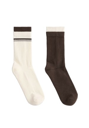 Ein Paar gerippte Socken, eins cremefarben mit braunem Bündchen und Streifen, eins einfarbig braun mit cremefarbenem Bündchen, flach auf weißem Hintergrund liegend.