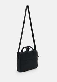 Sac messager noir avec une forme structurée, en matériau texturé, doté d'une longue bandoulière réglable et de deux poignées supérieures pour le transport.