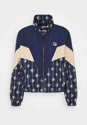 La giacca a vento navy e beige presenta una chiusura con zip, un colletto alto e un motivo geometrico del logo sulla parte inferiore e sulle maniche.