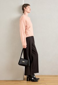 Pull en maille rose clair, pantalon large noir, bottines en cuir noires, et un sac à main structuré noir avec un accent doré.