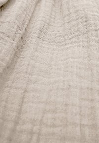 Helle beigefarbene Stoff mit einer strukturierten, zerknitterten Oberfläche, die subtile Muster und ein weiches, gewebtes Aussehen aufweist.