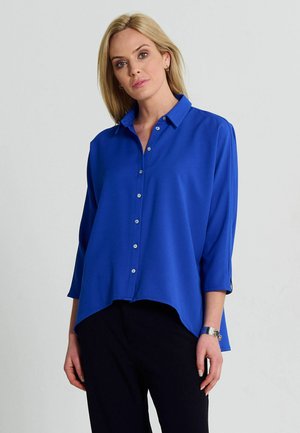 Blue blouse with a collared neckline, button detail, and three-quarter sleeves. Smooth texture with a slightly longer back hem.