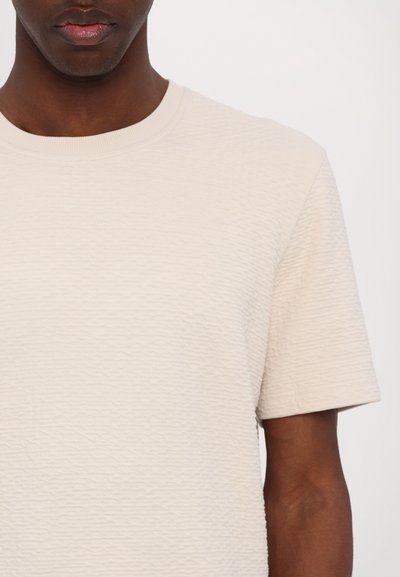 Lichtbeige textuurshorts met korte mouwen en een ronde hals, met een subtiel golvend patroon en een soepele stof.