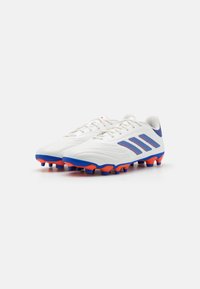Scarpe da calcio bianche con accenti blu e arancio, dotate di una tomaia testurizzata, tre strisce blu sul lato e una suola in gomma con più tacchetti.