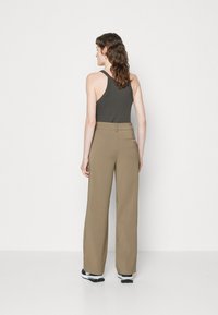 Lätta, khaki höga byxor med vid benformation, kombinerat med en åtsittande mörk tanktopp. Slät yta med minimala sömmar.