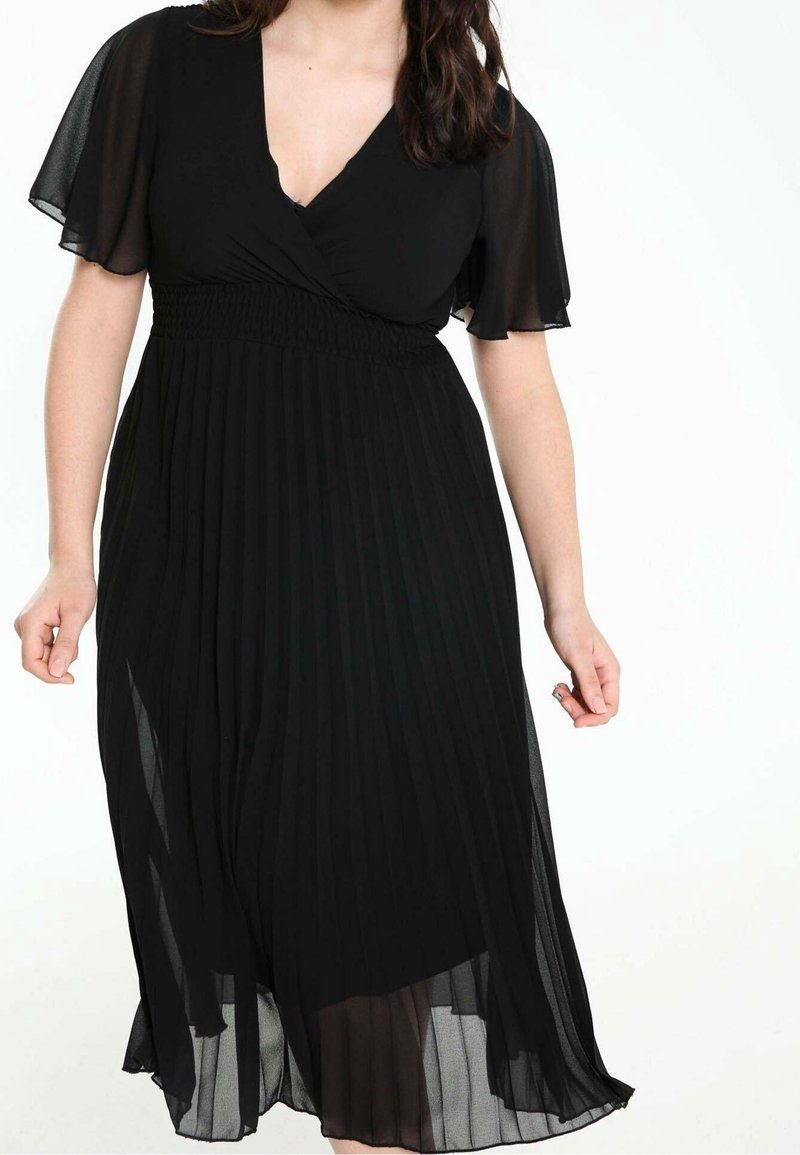 Robe noire plissée avec un col en V et des manches courtes transparentes. Le tissu présente une texture lisse avec un corsage ajusté et une jupe fluide.