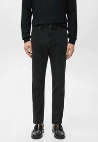 Pantalones vaqueros negros de corte ajustado, hechos de mezclilla. Presentan cinco bolsillos, cierre de botón y detalles mínimos de costura. Se llevan con zapatos negros.