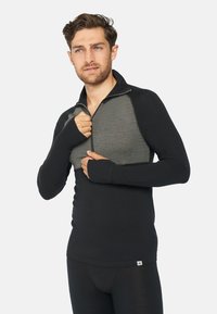 Schwarzes Langarmoberteil mit einem grauen Frontpaneel und einem halben Reißverschlussdesign. Verfügt über Daumenlöcher und eine figurbetonte Silhouette. Etikett am unteren Saum sichtbar.