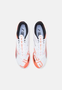 White athletic shoes with orange accents, mesh upper, textured design, flat laces, and black inner lining; features logo on tongue and side.