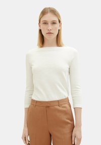 Haut long à manches blanches avec un col bateau, associ�é à un pantalon taille haute marron. Le tissu semble texturé et léger.