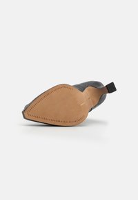 Suela de zapato de cuero negro con textura suave, tacón rectangular y fondo marrón claro que presenta un patrón de costura triangular y una línea central.