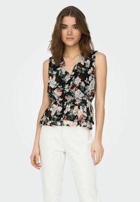 Blusa peplum floral en negro con estampados de rosas multicolores y hojas, con un profundo escote en V y diseño sin mangas. Combinada con pantalones blancos.
