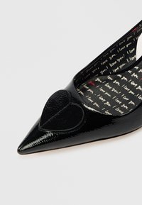 Sapatilha preta de bico fino em couro envernizado com um detalhe em forma de coração texturizado na parte da frente e interior com padrão apresentando o texto "Amo-te".