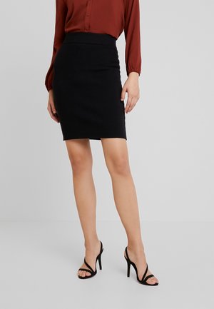 Jupe crayon noire avec une silhouette ajustée, fabriquée dans un matériau lisse. Associée à des sandales à talons hauts noires à fines brides et un chemisier couleur rouille.