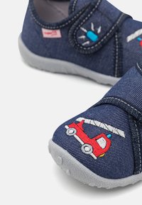 Modri denim natikači z sivo gumo, z rdečim vezenim dizajnom gasilskega vozila in luči. Zaponka na ježka za enostavno obuvanje.