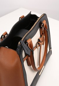 Borsa nera e beige con dettagli marroni; pelle texturizzata, ferramenta color oro, chiusura con zip, doppi manici e tasche interne.