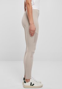 Bež helanke od rastezljivog materijala, s bočnim mrežastim panelima i uskim krojem. Uparene s bijelim tenisicama sa zelenim detaljima.