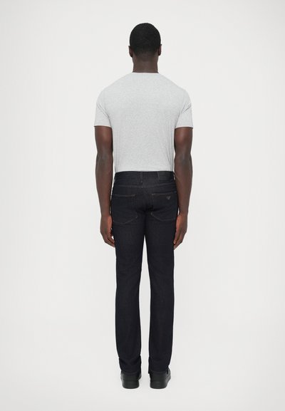Sivé tričko s krátkymi rukávmi v kombinácii s tmavými džínsami z denimu. Džíny majú textúrovaný povrch a jemné švy.