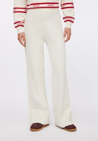 Pantaloni in maglia color bianco sporco, con gambe larghe, orlo a coste e texture liscia. Abbinati a scarpe bordeaux scuro.