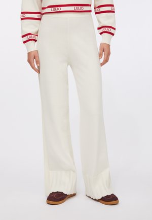 Pantaloni in maglia color bianco sporco, con gambe larghe, orlo a coste e texture liscia. Abbinati a scarpe bordeaux scuro.