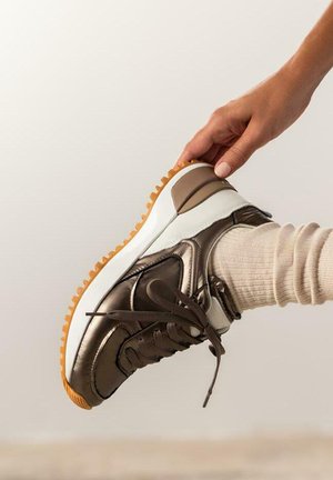 Zapatilla de cuero marrón con acentos blancos y suela de goma texturada, que presenta cordones marrones y un collar acolchado.