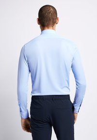 Lichtblauw langemouwen shirt met een kraag, zachte textuur en knoopdetails bij de manchetten, gecombineerd met donkere marineblauwe broeken.