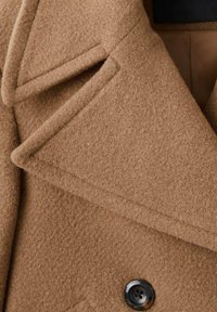 Cappotto di lana marrone con rever a lancia e bottone nero. Caratterizzato da un tessuto morbido e testurizzato e da dettagli di cuciture intricate.