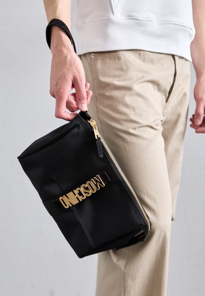 Melns auduma maisiņš ar zelta rāvējslēdzēju un zelta "MOSCHINO" logotipu uz melnas siksnas. Taisnstūra forma, gluda tekstūra.