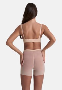 Reggiseno nudo con spalline regolabili e chiusura a gancio, abbinato a pantaloni corti nudi senza cuciture e trasparenti, che riflettono una texture liscia e leggera.