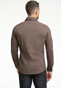 Camisa marrón de manga larga con cuello, fabricada en un tejido texturizado y con puños abotonados. Ajuste entallado, dobladillo curvado y diseño minimalista.