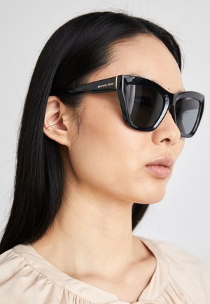 Svarta överdimensionerade solglasögon med kantiga bågar, med en glansig yta och guld "Michael Kors"-logotyp på sidan.