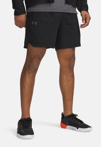 Černé sportovní šortky s jemným logem, doplněné černými a oranžovými teniskami se strukturovanými povrchy a kontrastními barvami.