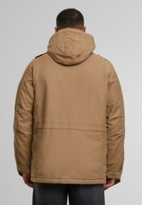 Chaqueta caqui con capucha, de corte recto, con costuras visibles y detalles en las costuras laterales. Textura suave, diseño informal y sin forrar.