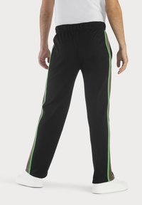 Schwarze Sporthose mit grünen Seitenstreifen, elastischem Bund und lockerer Passform. Der Stoff wirkt weich mit einem leichten Glanz.