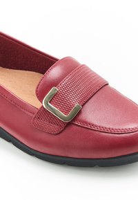 Mocassino in pelle rossa con una fascia testurizzata, messa in risalto da una fibbia dorata. Caratterizzato da una soletta imbottita e suola in gomma nera.