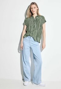 Zielono-biała, paskowana koszula z krótkim rękawem i kołnierzykiem, zestawiona z jasnoniebieskimi szerokimi spodniami i białymi trampkami. Gładka tekstura tkaniny.