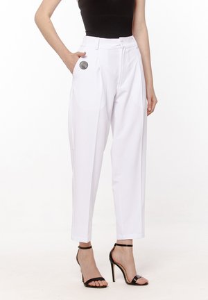 Białe spodnie o dopasowanym kroju i luźnym fasonie, z czarnym okrągłym akcentem na biodrze, wykończone mankietami. Czarne sandały na wysokim obcasie.