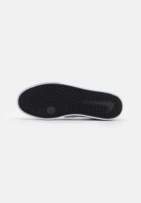 Balta sporta apavu zole ar strukturētu melnu gumijas virsmu, kas satur zigzaga rakstu un centrālo zvaigznes detāli. Klāt ir Nike logo.