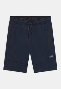 Marineblå shorts laget av mykt stoff, med to glidelås-lommer på siden, strammemansjett med snøring, og et lite merke på benet.
