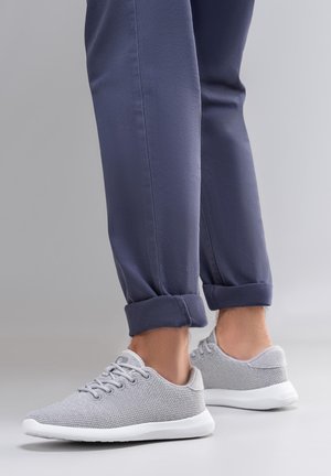 Jasnoszare dzianinowe tenisówki z białymi podeszwami, okrągłymi sznurowadłami i teksturowanym siateczkowym wierzchem. Nosi się je z podwiniętymi granatowymi spodniami, prezentując casualowy styl.